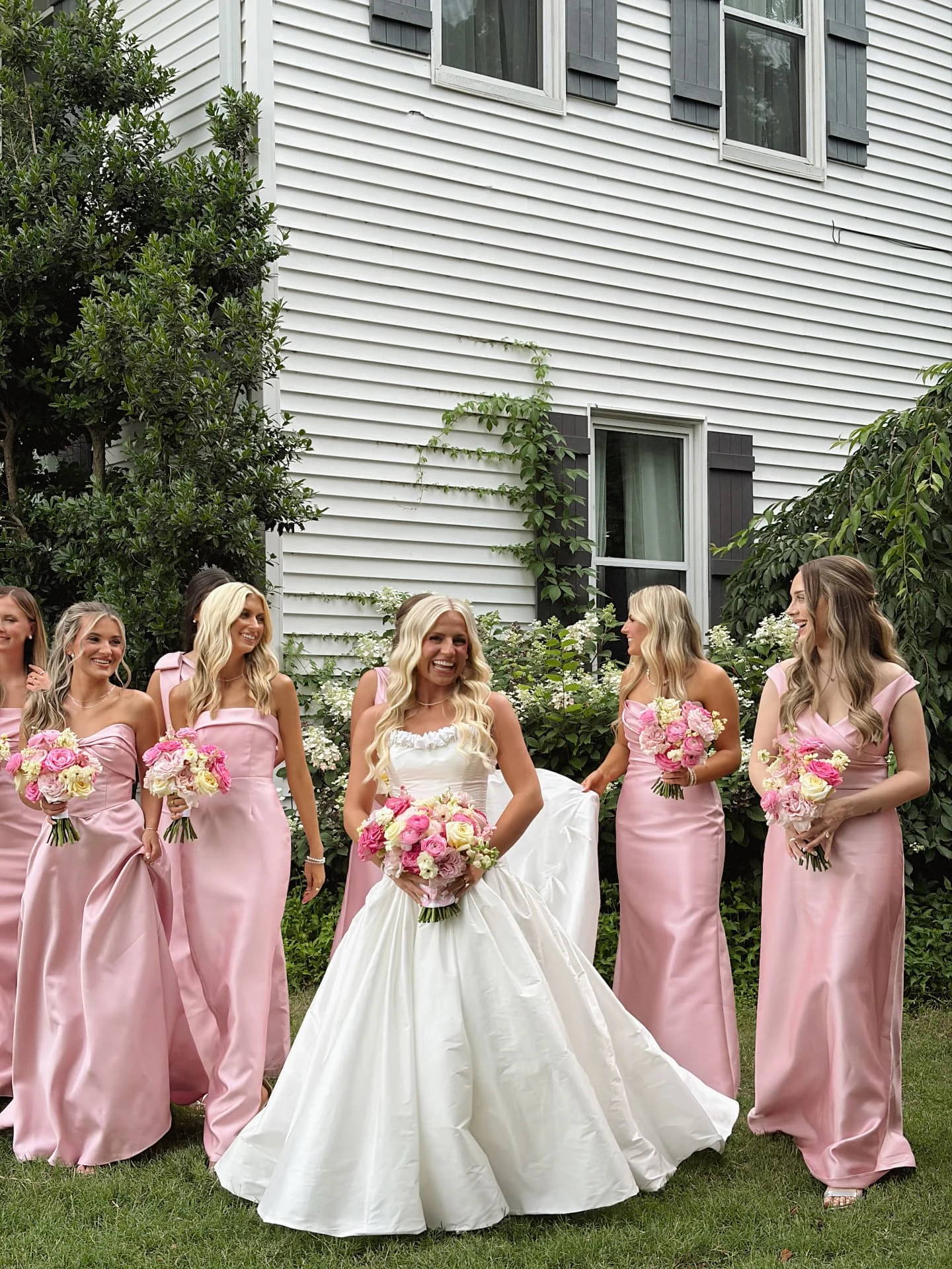 Bride and bridesmaids in pink dresses outside a white house